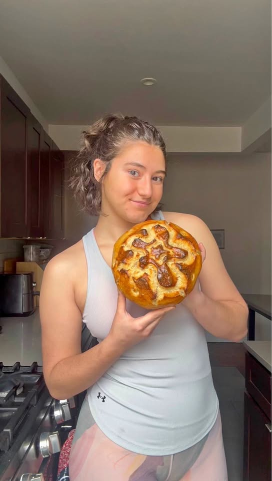 Persephone holding a fresh homemade sourdough loaf with custom scoring